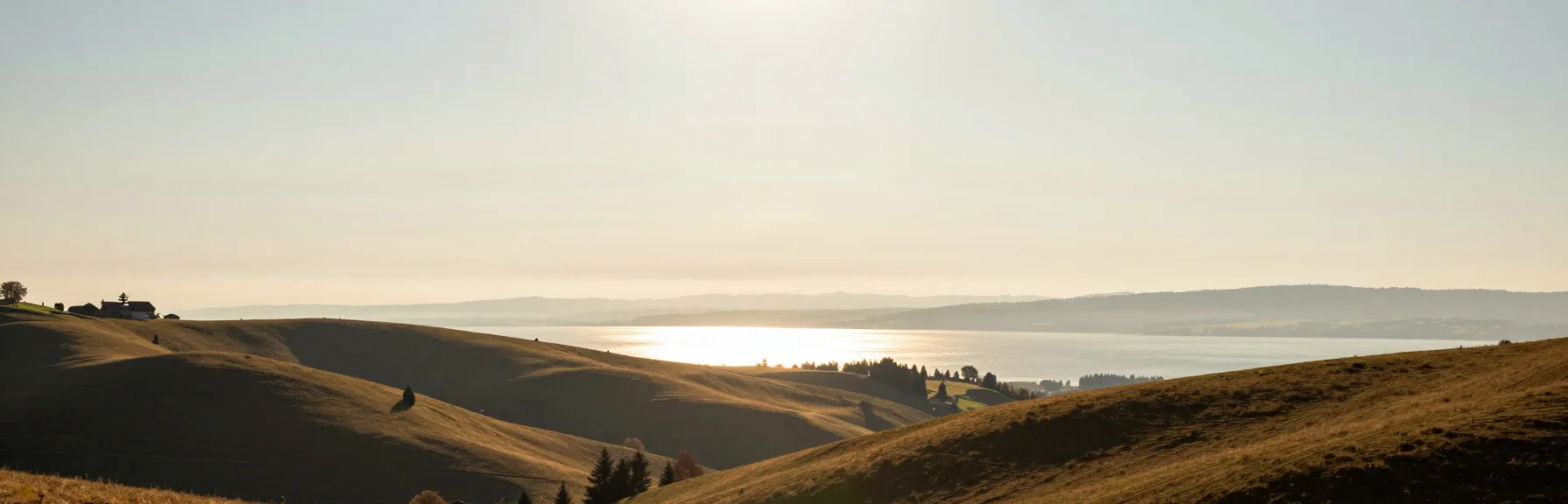 Weite Hügellandschaft im Abendlicht mit See am Horizont — KI-generierte Szene